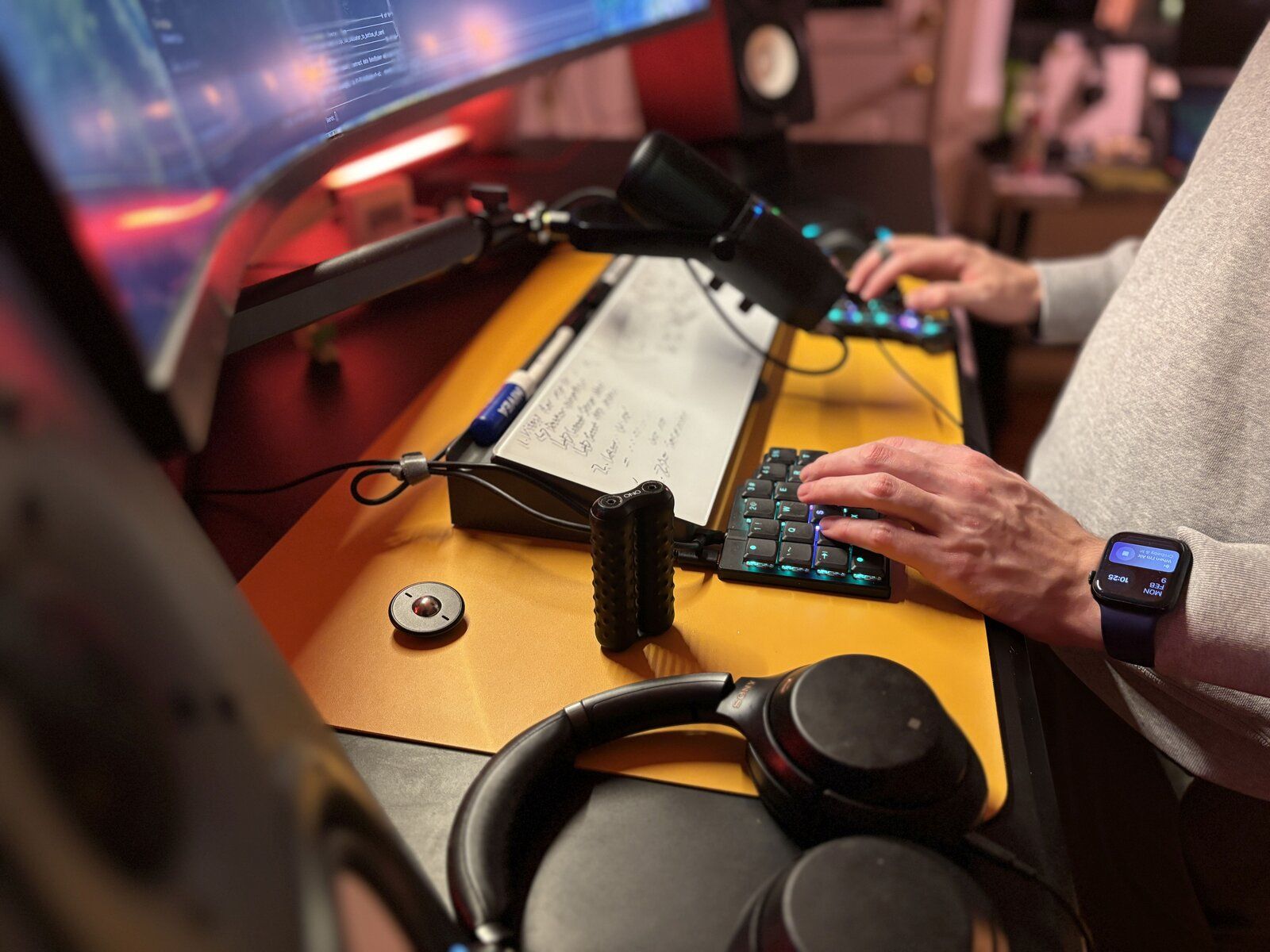 Close-up of Simon typing on the backlit ZSA Voyager split keyboard, with a desk-arm mic, fidget toy and headphones nearby